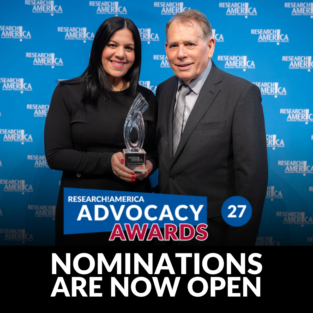 Research!America Advocacy Awards promotional graphic featuring two award attendees standing in front of a blue Research!America step-and-repeat backdrop. One person holds a glass award while posing beside another attendee in a suit. Overlay text reads: “Research!America Advocacy Awards,” “27,” and “Nominations Are Now Open.”
